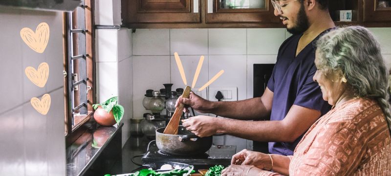 Woman with grey hair in orange top helps a man in a blue top cook in the kitchen